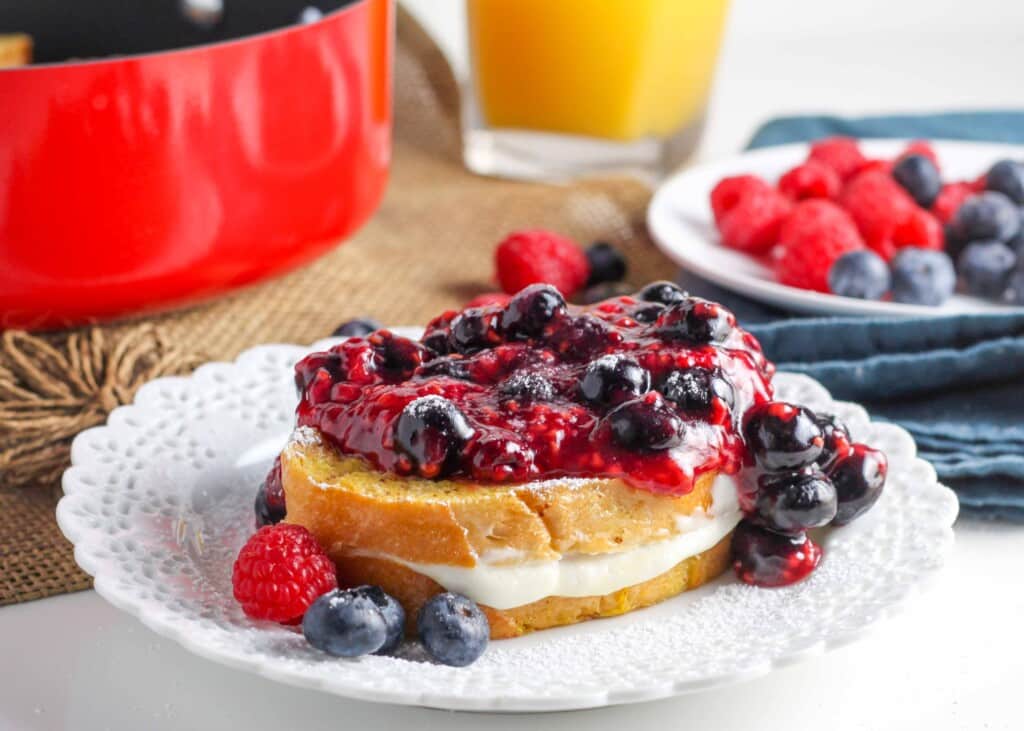 French toast with cheesecake filling and berry sauce on top on white plate