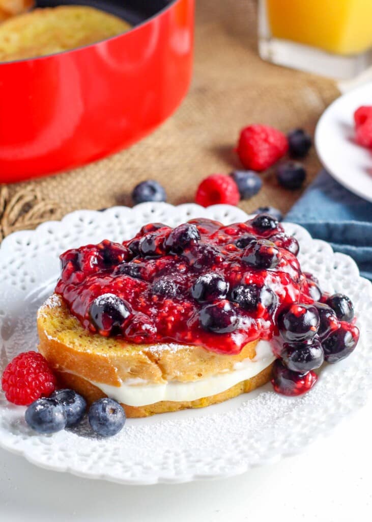 french toast with berries and cheesecake filling on frilly white plate