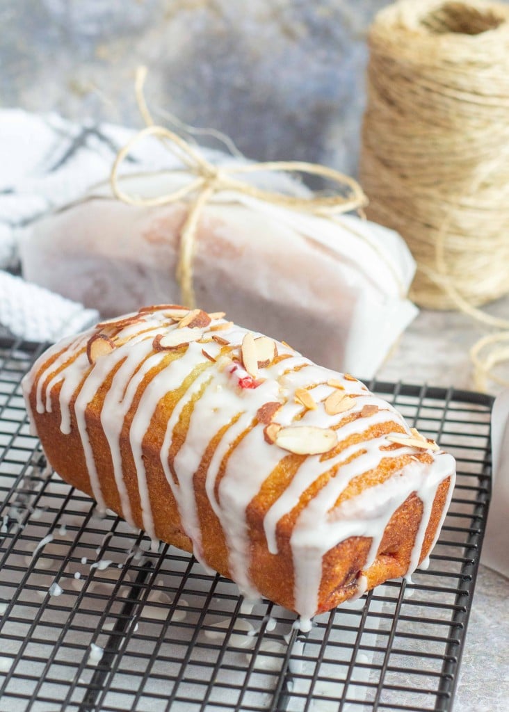 a loaf of cherry almond bread, drizzled with a glaze cools on a black wire rack