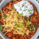 chili in bowl with cheese, sour cream, and cilantro