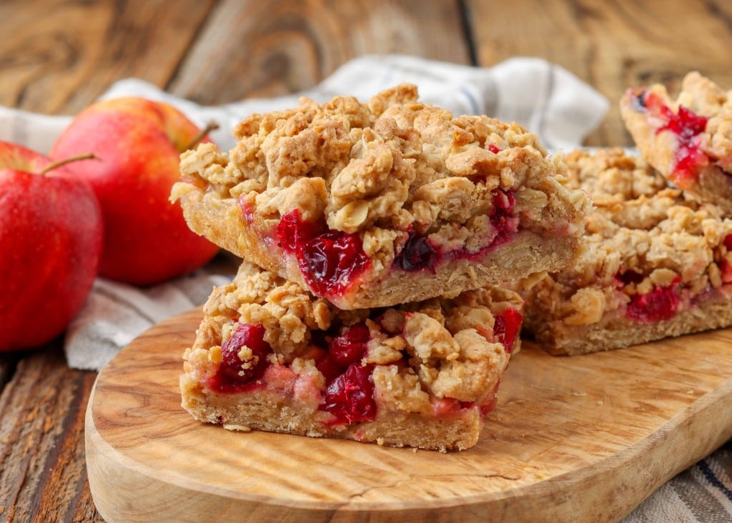stacked Cranberry Apple Crumb Bars with apples in background