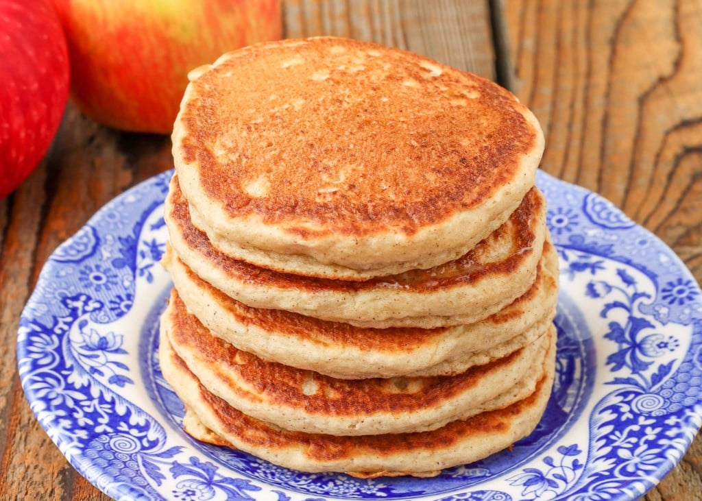 pancakes stacked on small blue plate next to apples