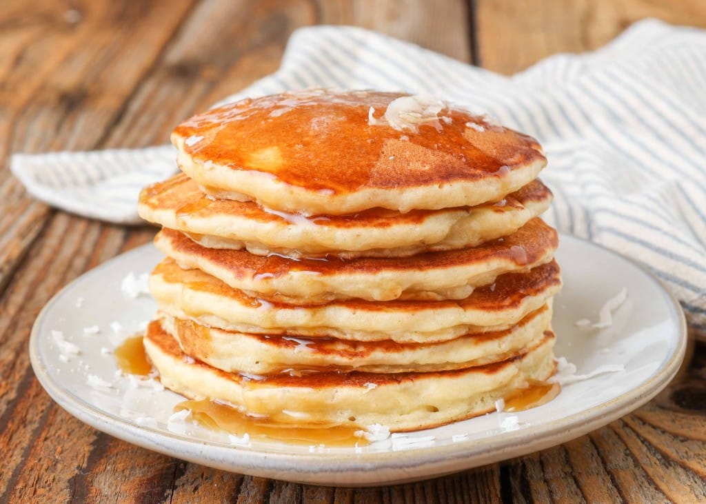 Banana Coconut Pancakes stacked on plate with syrup