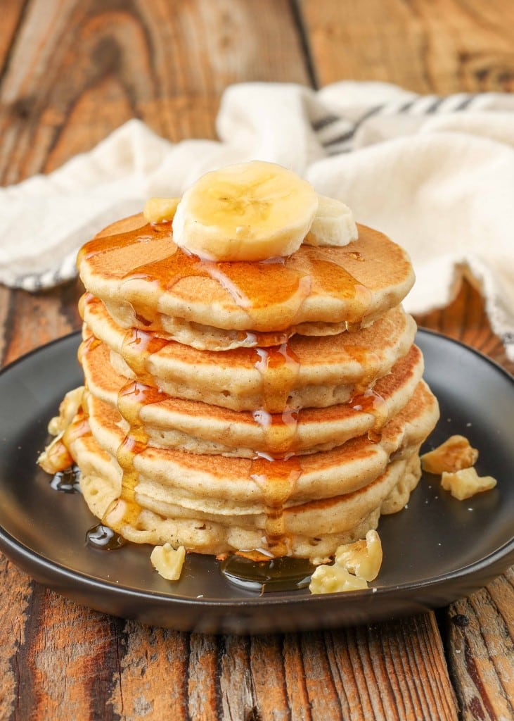stacked pancakes on small black plate with bananas on top