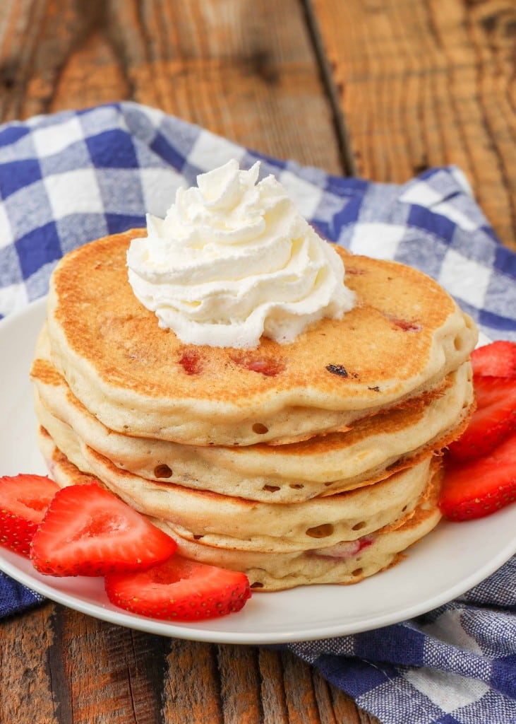 Strawberry filled pancakes stacked with berries on the side 