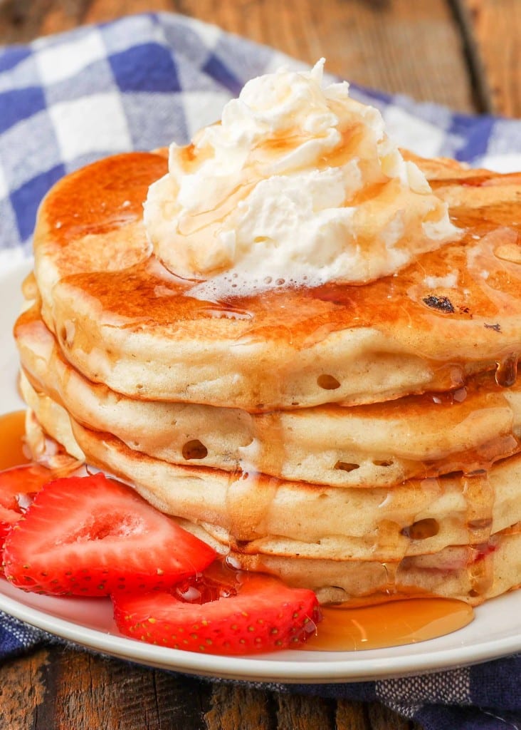 Pancakes filled with strawberries topped with whipped cream and syrup