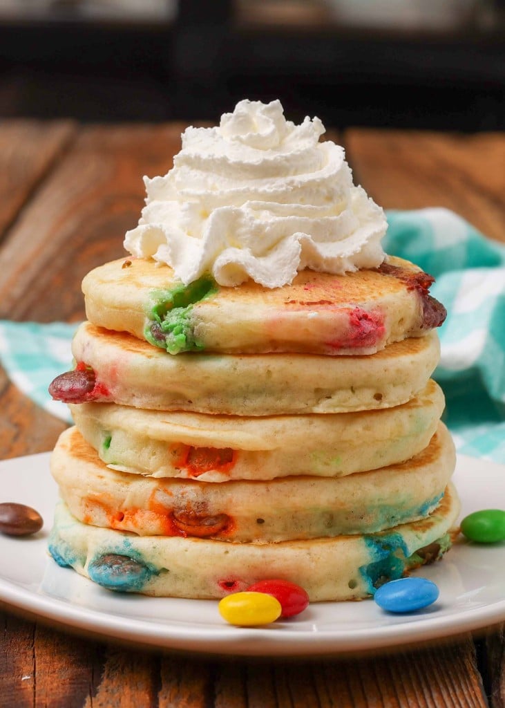 pancakes with M&Ms and whipped cream stacked on small square plate