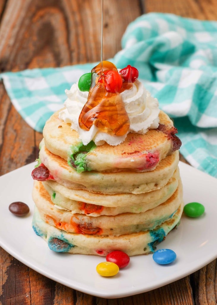 M&M Pancakes with whipped cream and syrup on square plate