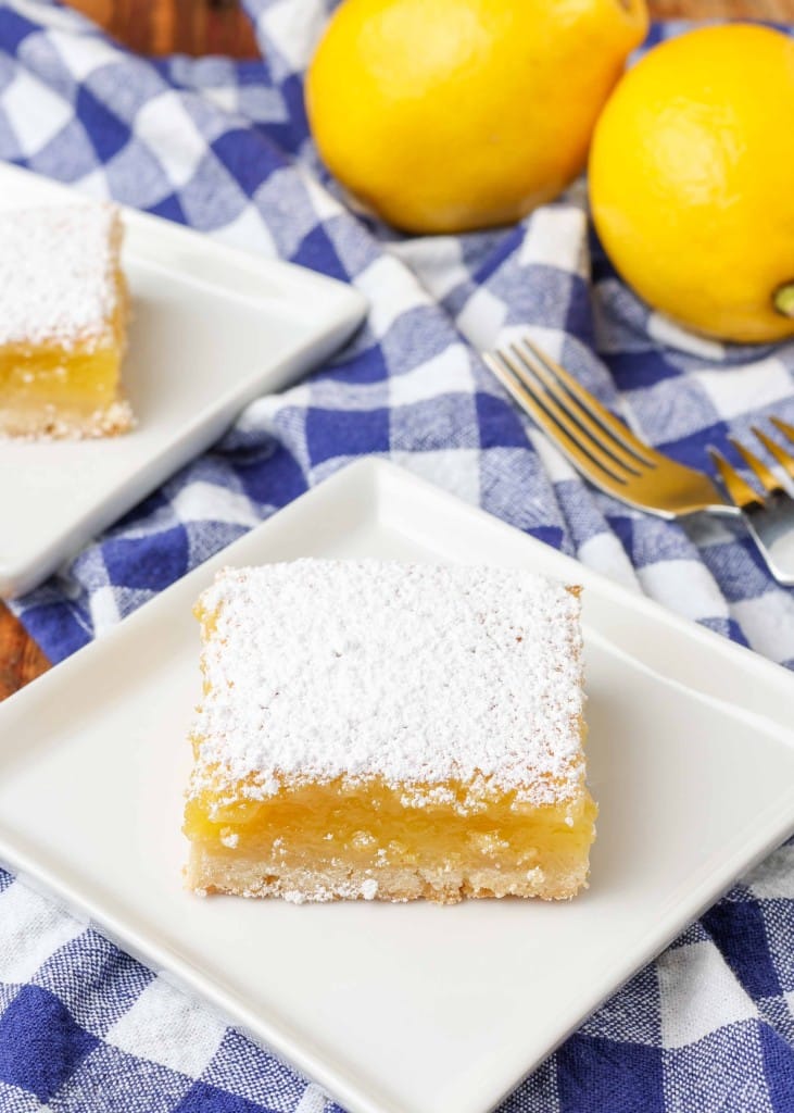 lemon bar on small white plate with blue and white napkin and fork