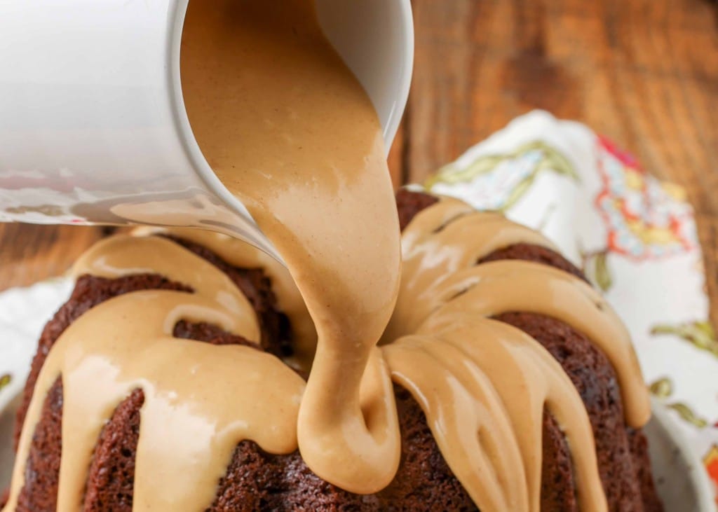 a close up shot of peanut butter being poured from a white pitcher with the cake in the background