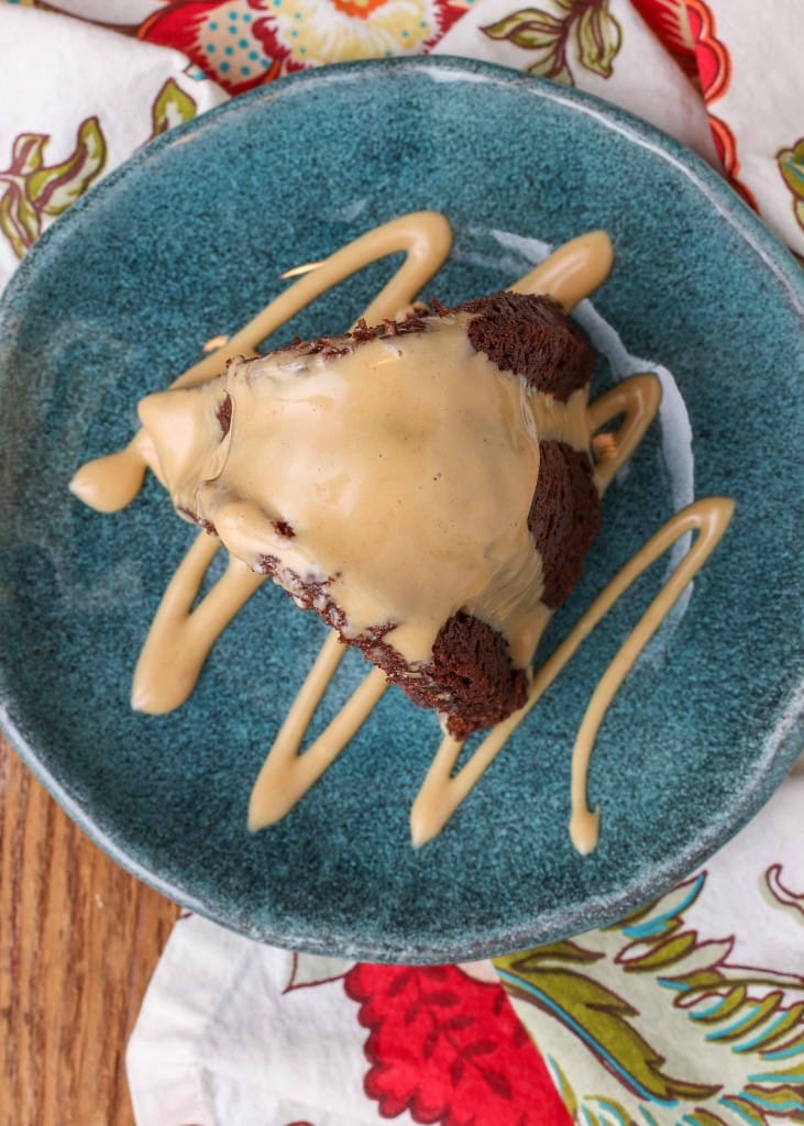 a top down photo of a slice of chocolate cake standing on a blue ceramic plate. the plate and the cake have been artistically drizzled with a light brown peanut butter glaze