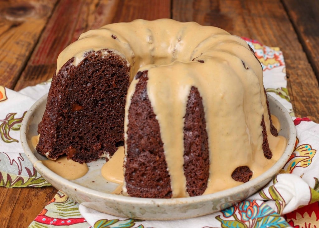 moist chocolate bundt cake with one slice missing, drizzled with peanut butter glaze on a speckled white plate