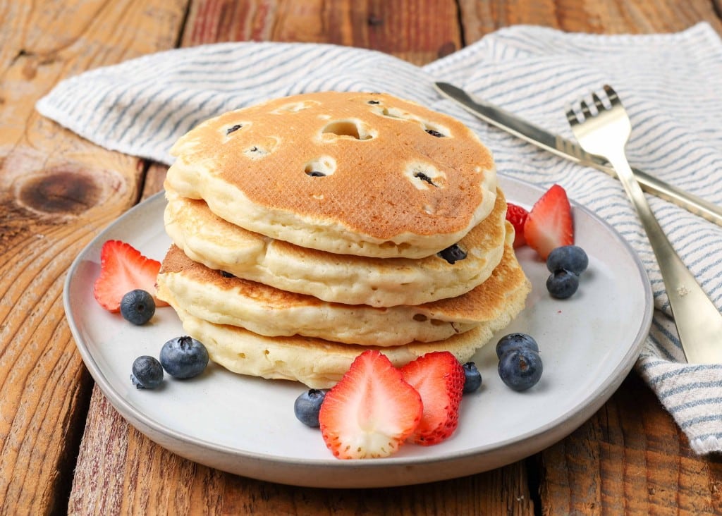 thick and fluffy berry pancakes on a white plate on a wooden tabletop with a napkin nearby