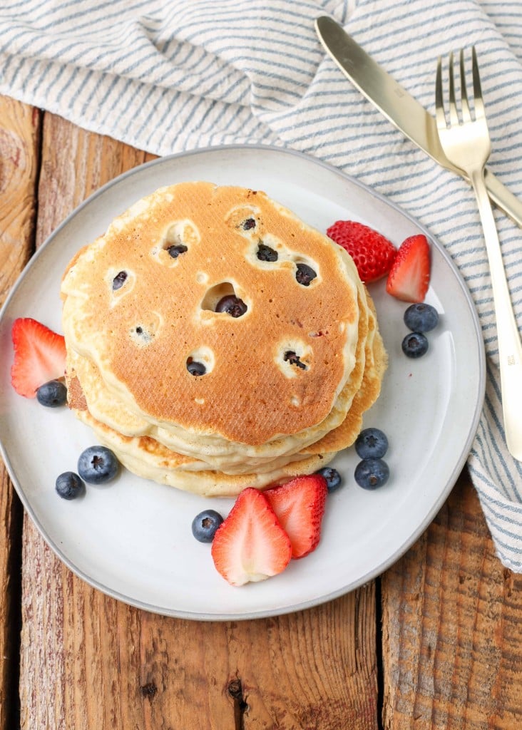 a top down shot of a white plate with a stack of blueberry and strawberry pancakes on it, with more berries on the plate