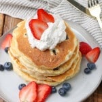 sliced strawberries and fresh blueberries have been placed atop and around this stack of fresh berry pancakes topped with whipped cream