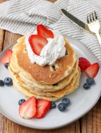 sliced strawberries and fresh blueberries have been placed atop and around this stack of fresh berry pancakes topped with whipped cream