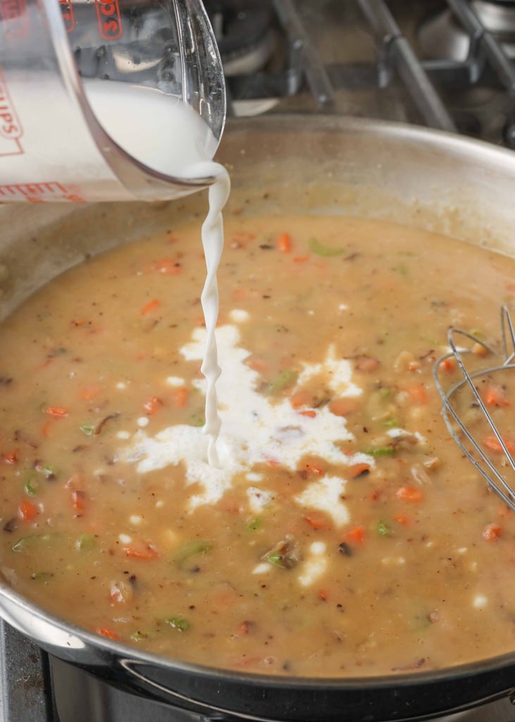 Pouring milk into the gravy with the vegetables to make the chicken pot pie filling in a metal skillet