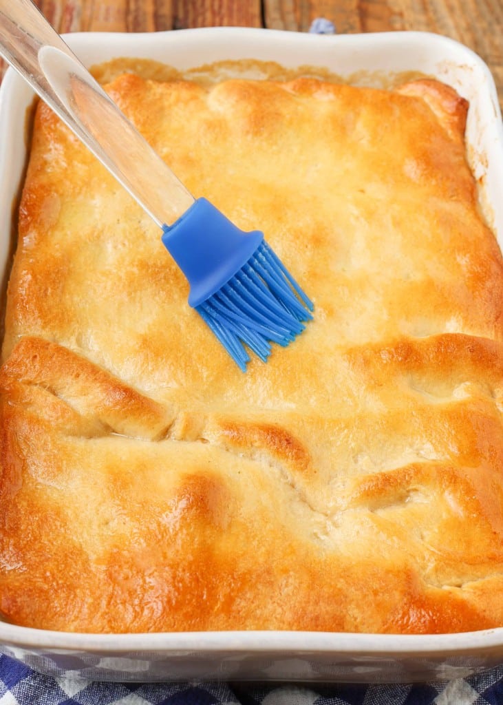 brushing butter onto the golden crisp crust of a chicken pot pie in a white 9x13 baking dish