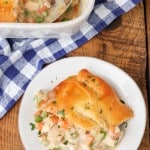a top down photo of a serving of crescent roll chicken pot pie on a white plate on a wooden tabletop