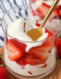 a vertical photo of a ball glass with layers of sweet cream and strawberries visible inside