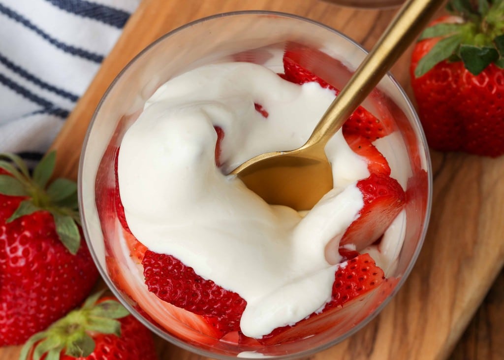 a top down photo looking into a glass filled with strawberries and cream. there is a gold plated spoon resting in the strawberries and cream.