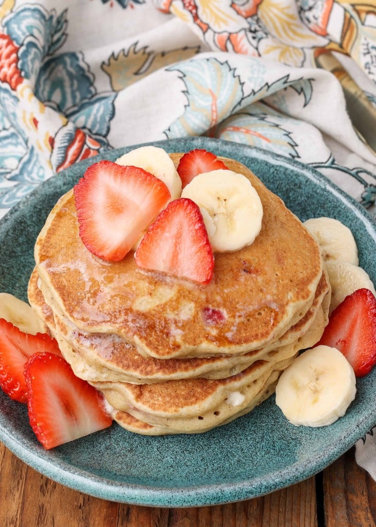 fruit pancakes stacked on plate with berries and bananas