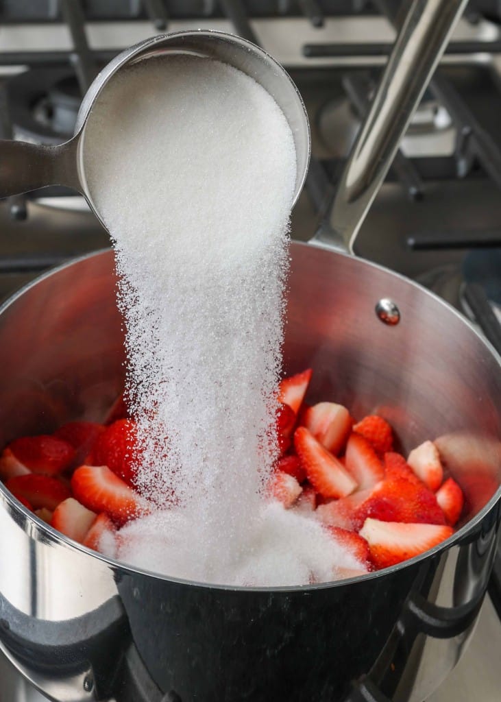 Strawberry Compote sugar pouring into saucepan of strawberries