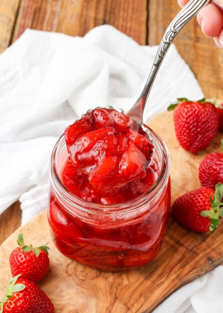 Strawberry Compote in glass jar with spoon and fresh berries