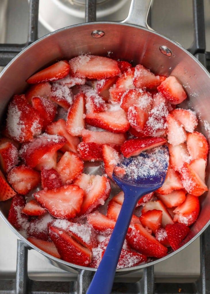 strawberries and sugar in sauce pan with blue spatula