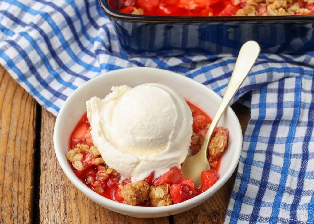 bowl of strawberry crisp with ice cream on a blue and white checked cloth