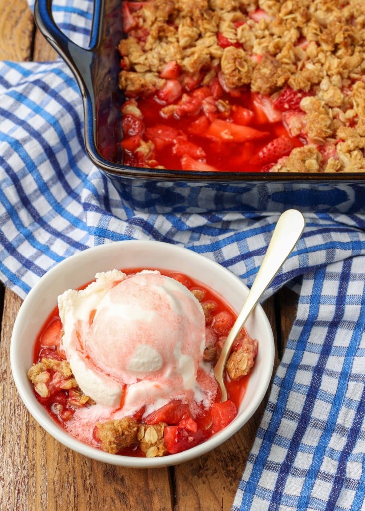 bowl of strawberry crisp with ice cream on a blue and white checked cloth