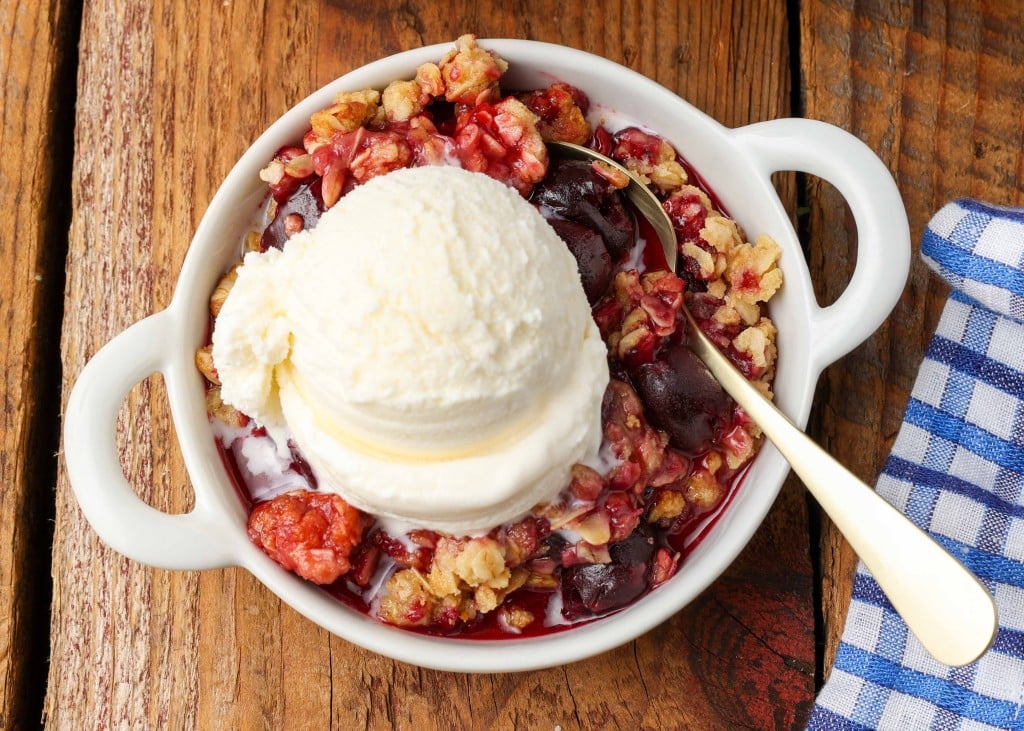 Fruit crisp with ice cream in white dish with silver spoon and blue napkin