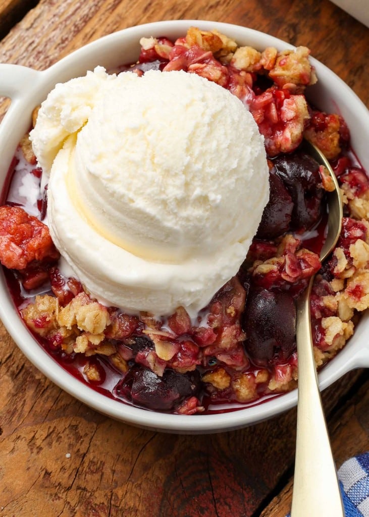Cherry Crisp topped with vanilla ice cream in white bowl with gold spoon