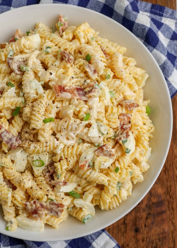 Overhead vertical shot of bacon pasta salad, served on an off-white platter