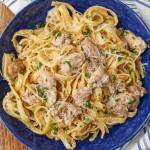 Overhead horizontal shot of garlic chicken parmesan pasta, served in a blue bowl with a striped gray and white towel