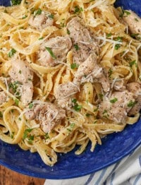 Overhead close-up shot of garlic parmesan chicken pasta in a blue bowl with a striped gray and white towel