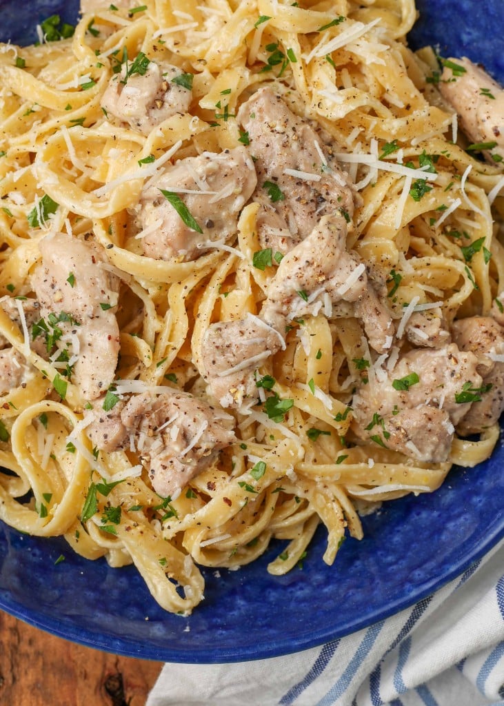Overhead close-up shot of garlic parmesan chicken pasta in a blue bowl with a striped gray and white towel