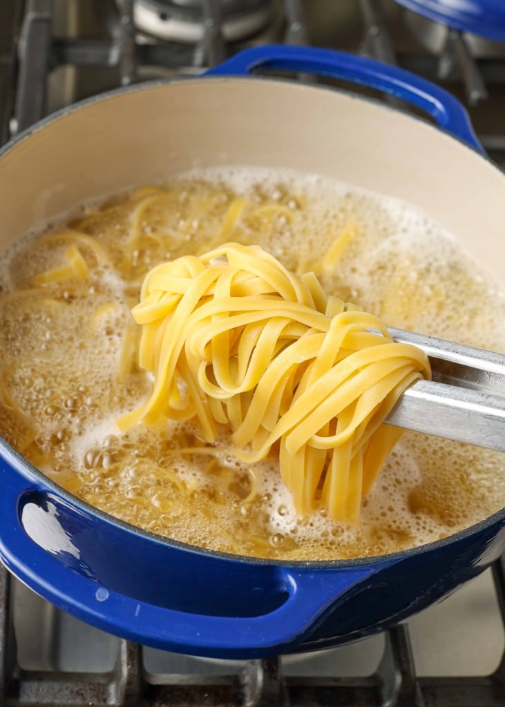 Overhead shot of pasta cooking in a blue pot, held up for the camera by silver tongs
