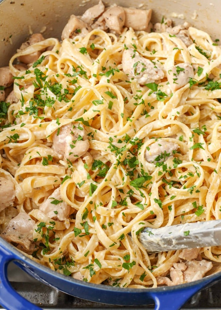 Close-up shot of garlic parmesan chicken pasta in a blue dish, stirred with silver tongs
