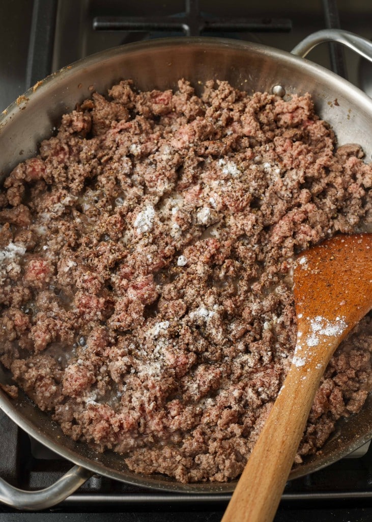 Overhead shot of ground beef cooking in a stainless steel skillet, with a wooden spoon