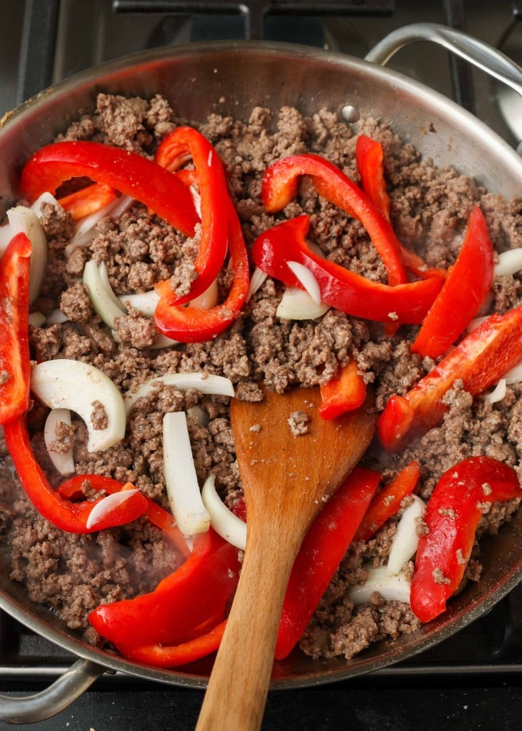 Overhead shot of ground beef, red bell peppers, and yellow onions cooking in a stainless steel skillet