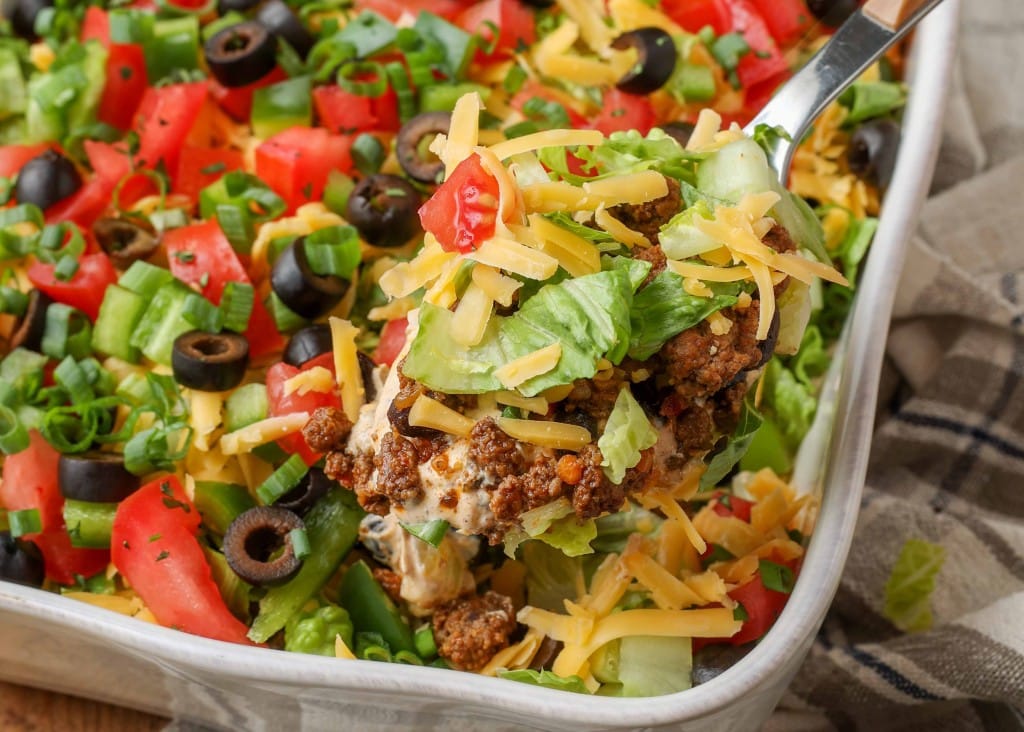 Layered taco dip with beef, beans, lettuce, tomato, olives, cheese, and sour cream
