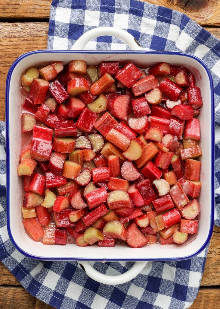 Overhead vertical shot of cobbler filling with plenty of rhubarb in a square white baking dish with blue borders, on a checkered blue and white hand towel