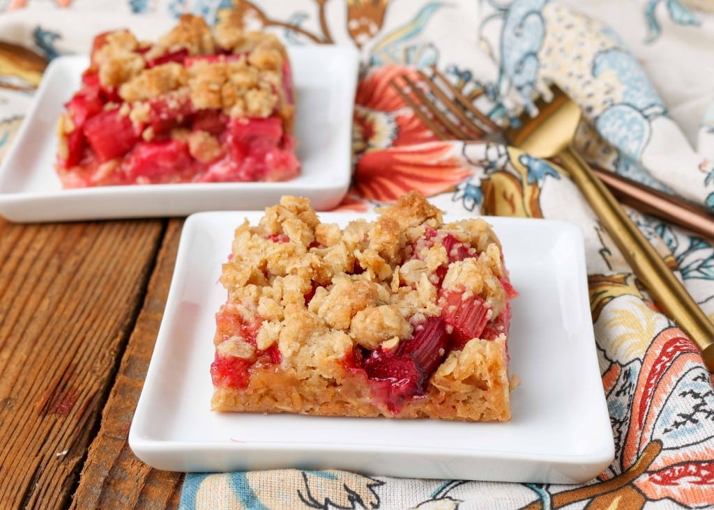 Rhubarb bars with crunchy oatmeal topping, served on a square white plate with a golden fork and floral print towel