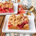 Rhubarb bars with crunchy oatmeal topping, served on a square white plate with a golden fork and floral print towel