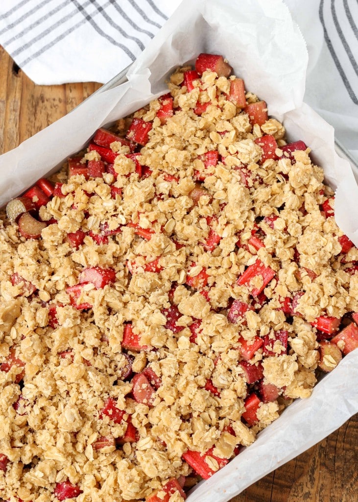 Overhead shot of rhubarb oatmeal bars prepared in a sheet pan lined with parchment paper, ready to bake