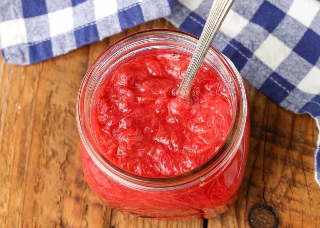 fresh rhubarb sauce in jar with silver spoon next to blue checkered napkin
