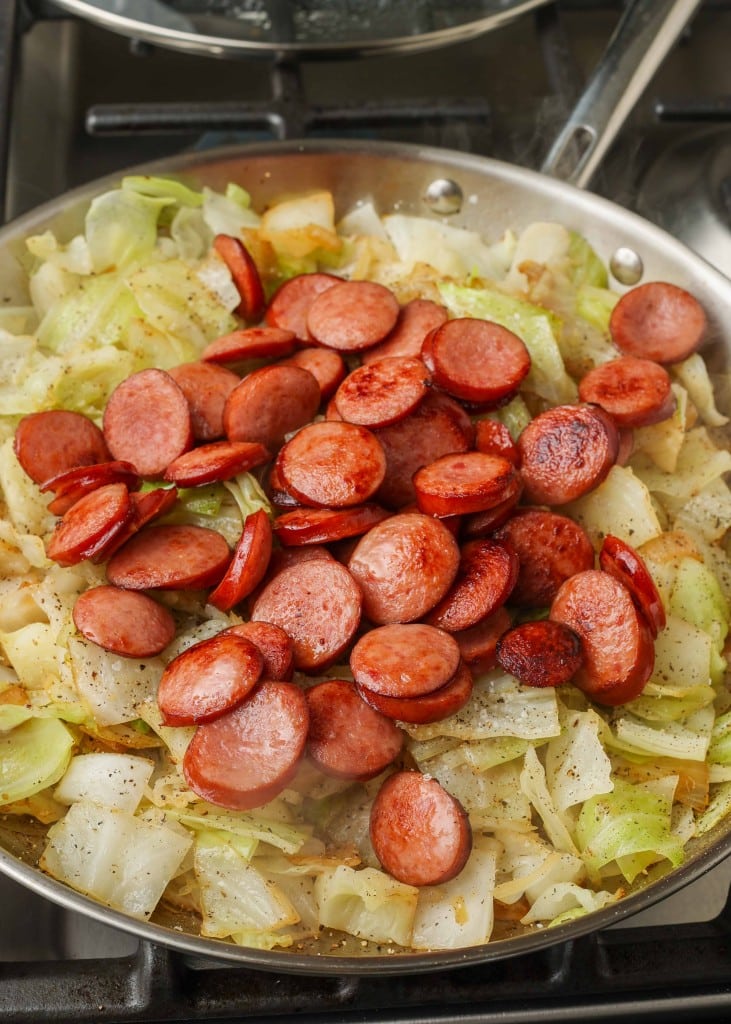 Lettuce, garlic, kielbasa, and onions in a stainless steel skillet