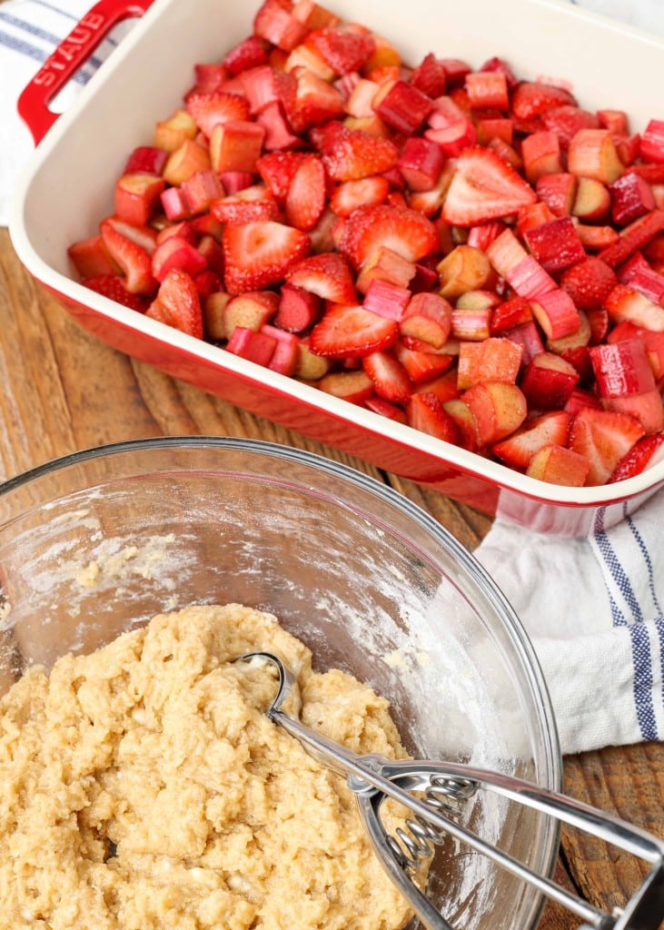 a bowl containing the mixed flours and spices for the crust is placed beside the baking dish full of chopped berries and rhubarb