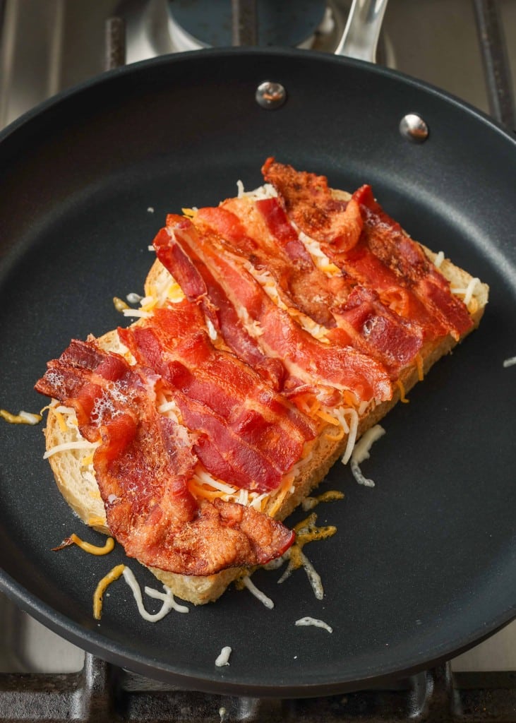 cheese and bacon have been layered atop one slice of bread in the non-stick pan